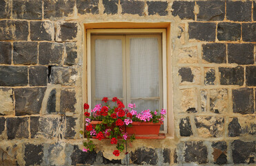 Stone house, window and blooming geranium