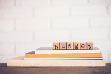 The word Budget, alphabet on wooden rubber stamps on top of books and table. Bricks background,...