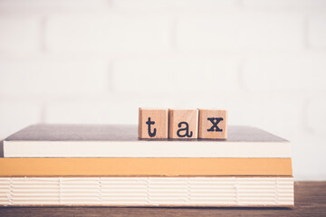 The word Tax, alphabet on wooden rubber stamps on top of books and table. Bricks background, blank...