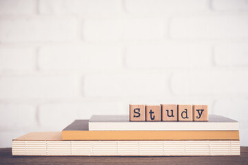The word Study, alphabet on wooden rubber stamps on top of books and table. Bricks background,...