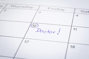 Closeup on calendar page, focus on blue handwriting the wordÂ Doctor written on timetable date 10th with circle mark. Personal health reminder, hospital schedule, appointment note, time management.