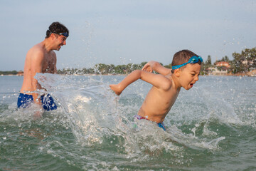 A boy around six is playing in the sea water with his father splashing.
