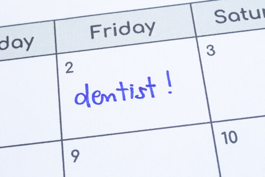 Closeup on calendar page, focus on blue handwriting the wordÂ Dentist written on timetable date 2nd under Friday column. Appointment note health reminder, schedule, personal time management.