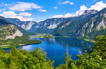Naklejka na ściany i meble Hallstatt, Austria. Top view to lake Hallstattersee among austrian Alps mountains and green trees in forest. Summery landscape sunny day with blue sky and clouds.