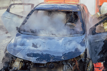 Firefighters extinguishing a burning car that caught fire in a city parking lot. Clouds of white smoke and steam. Incident in a parking lot in the city. Dangerous job