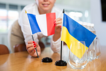 Preparation for international negotiations. Female office coordinator setting national flags of...