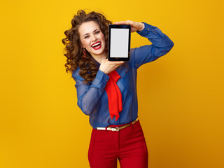 happy modern woman with long wavy brunette hair against yellow background showing tablet PC blank screen