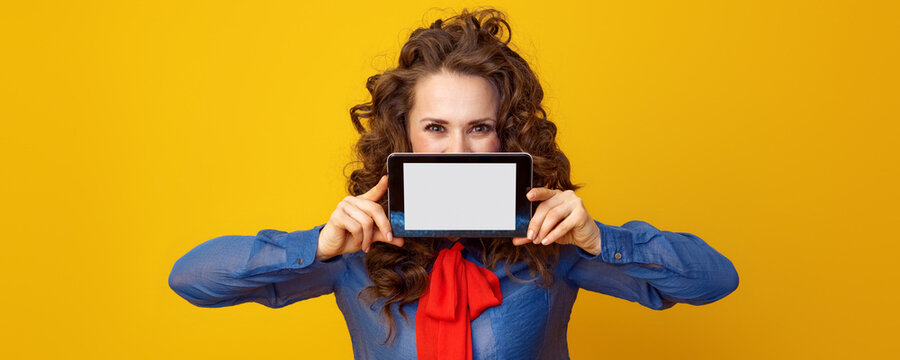modern woman with long wavy brunette hair hiding behind tablet PC blank screen on yellow background