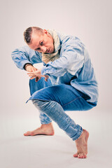 caucasian male dancer wearing blue denim shirt and pants on light background performing hip hop and contemporary style dance.