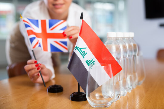 Female secretary places flags of the Iraq and United Kingdoom flag on the table before the negotiations of top political figures