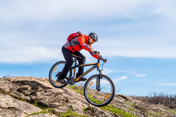 Cyclist in Red Jacket Riding the Mountain Bike Down Rocky Hill. Extreme Sport and Adventure Concept.