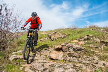 Cyclist in Red Jacket Riding the Mountain Bike Down Rocky Hill. Extreme Sport and Adventure Concept.