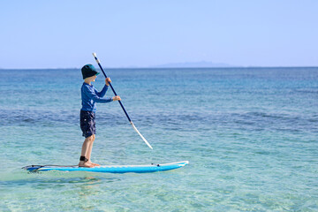 Fototapeta na wymiar cheerful little boy enjoying stand up paddleboarding alone, active vacation concept, copy space on right