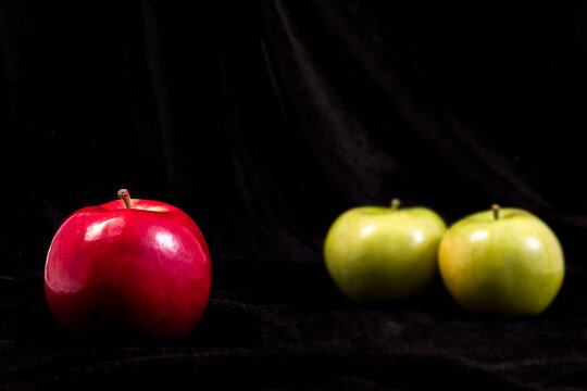 one red and two green apple on black background.