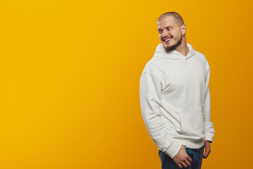 Young caucasian smiling pensive man wearing white hoodie looking aside at free empty space isolated on yellow background. People lifestyle concept