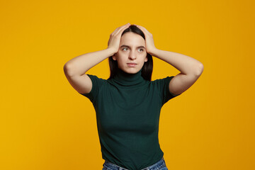 Photo of troubled girl holds hands on head and look in panic, standing distressed and shocked against yellow background