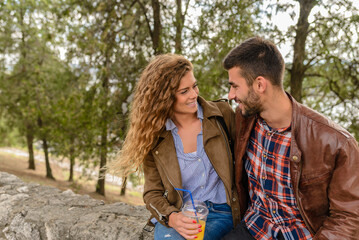 Fototapeta premium Young couple taking a rest after a long walk and refreshing with orange juice in the public park