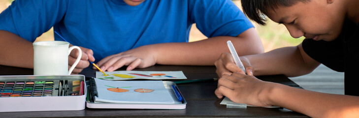 Closeup image of watercolor painting, drawing and coloring with watercolor on table of asian boys at home, cropped shot, concept for recreational activity of children around the world.