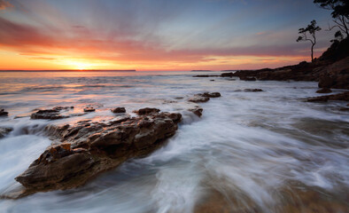 Fototapeta na wymiar Beautifuol sunrise over the bay as the ocean ebbs and flows gently over rocks at the shore edge
