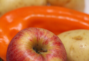 focus on the apple with orange bell pepper and potato in the background. natural food set with apple, potato and bell pepper.
