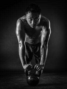 Photo Of A Muscular Asian Man Doing Pushups With A Kettlebell. Focus On His Face.