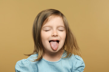 Funny little girl showing her tongue on beige background © New Africa