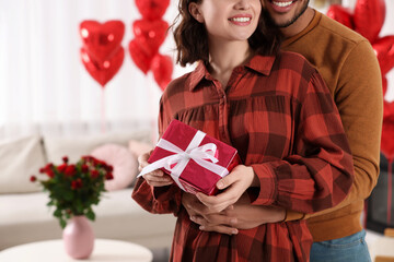 Happy couple celebrating Valentine's day. Beloved woman with gift box in room decorated with heart...