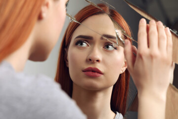 Sad young woman suffering from mental problems near broken mirror