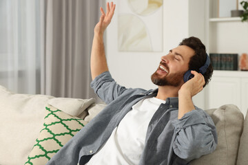 Happy man listening music with headphones on sofa indoors