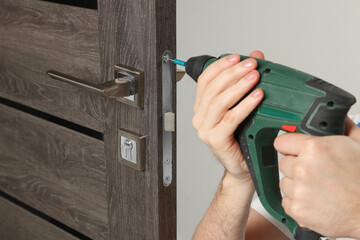 Worker with screw gun repairing door lock indoors, closeup