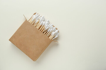 Box with wooden cotton buds on beige background, top view. Space for text