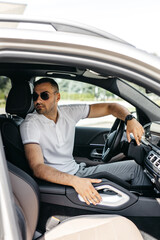 vertical photo of a young man in glasses driving a luxury car looking back at his passengers