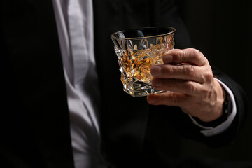 Man holding glass of whiskey with ice cubes on dark background, closeup