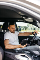 young businessman driving an expensive car reading his notebook