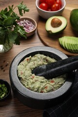 Delicious guacamole in mortar and ingredients on wooden table, closeup