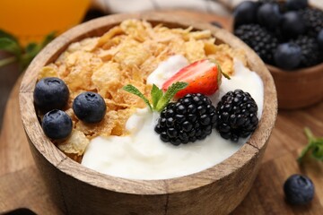 Delicious crispy cornflakes, yogurt and fresh berries in bowl on wooden board, closeup. Healthy breakfast