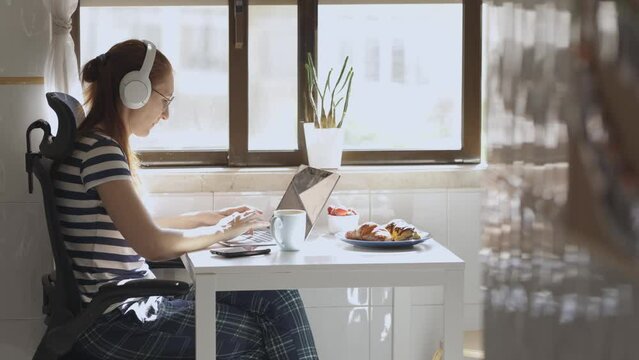 Woman work at home in headphones during breakfast