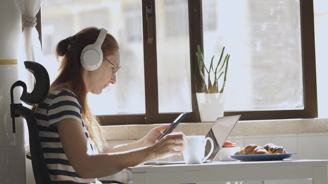 Woman at home at table with phone, laptop, coffee