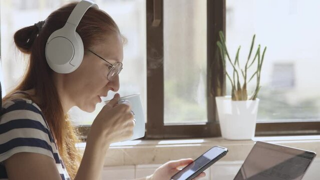 Woman in headphones drink coffee, watch on phone