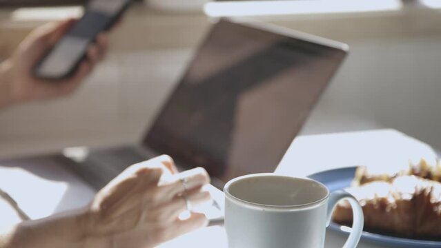 Cup of coffee, blurred hands with phone and laptop