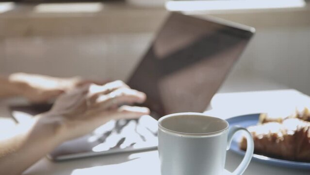 Steam in cup and blurry hands typing on a laptop
