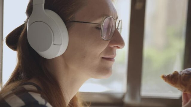 Woman in headphones eating a croissant, close-up