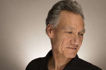 Portrait of a mature man with graying hair wearing a black shirt 60plus looking down