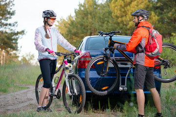 Fototapeta na wymiar Young Couple Preparing for Riding the Mountain Bikes in the Forest. Unmounting the Bike from Bike Rack on the Car. Adventure and Family Travel Concept.