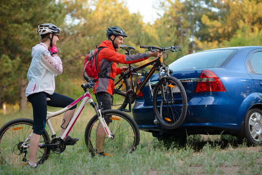 Young Couple Preparing for Riding the Mountain Bikes in the Forest. Unmounting the Bike from Bike Rack on the Car. Adventure and Family Travel Concept.