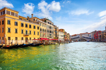 Venice, Italy. Panorama view at Rialto Bridge on Grand Canal in Venezia. Gondolas floating by piers docksamong antique buildings and traditional italian Venetian architecture. Sunny day with blue sky 