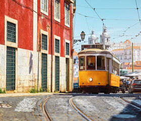 Naklejka na ściany i meble Lisbon, Portugal. Vintage yellow retro tram on narrow bystreet tramline. Red houses in Alfama district of old town. Popular touristic attraction of Lisboa city.