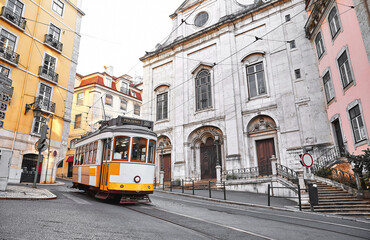Naklejka na ściany i meble Lisbon, Portugal. Vintage yellow retro tram on narrow bystreet tramline in Alfama district of old town. Popular touristic attraction of Lisboa city.