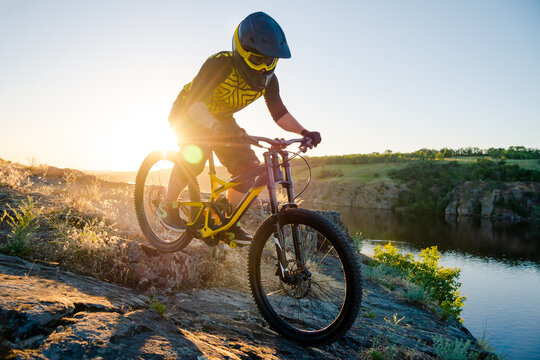Professional Cyclist Riding the Downhill Mountain Bike on the Summer Rocky Trail at the Evening. Extreme Sport and Enduro Cycling Concept.