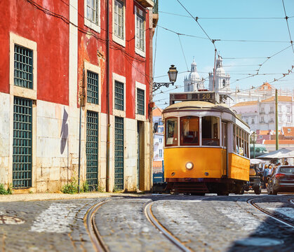 Lisbon, Portugal. Vintage yellow retro tram on narrow bystreet tramline. Red houses in Alfama district of old town. Popular touristic attraction of Lisboa city. © Designpics